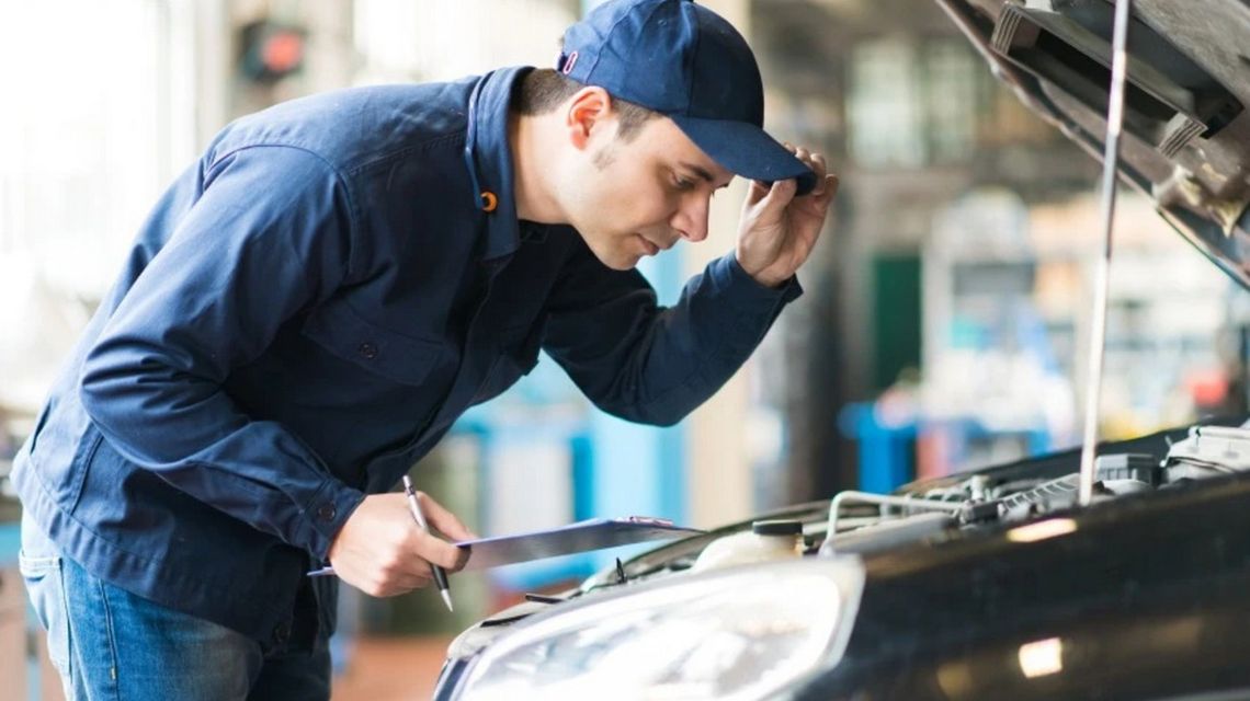 zdjęcie przedstawia mężczyznę nachylającego się nad silnikiem w samochodzie