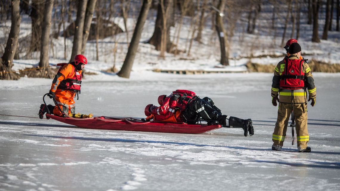 zdjęcie przedstawia strażaków na saniach, którzy jadą po lodzie