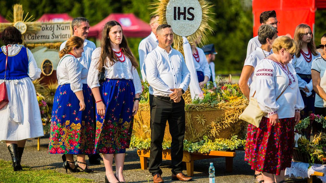 zdjęcie przedstawia ludzi w strojach ludowych przy dożynkowym wieńcu