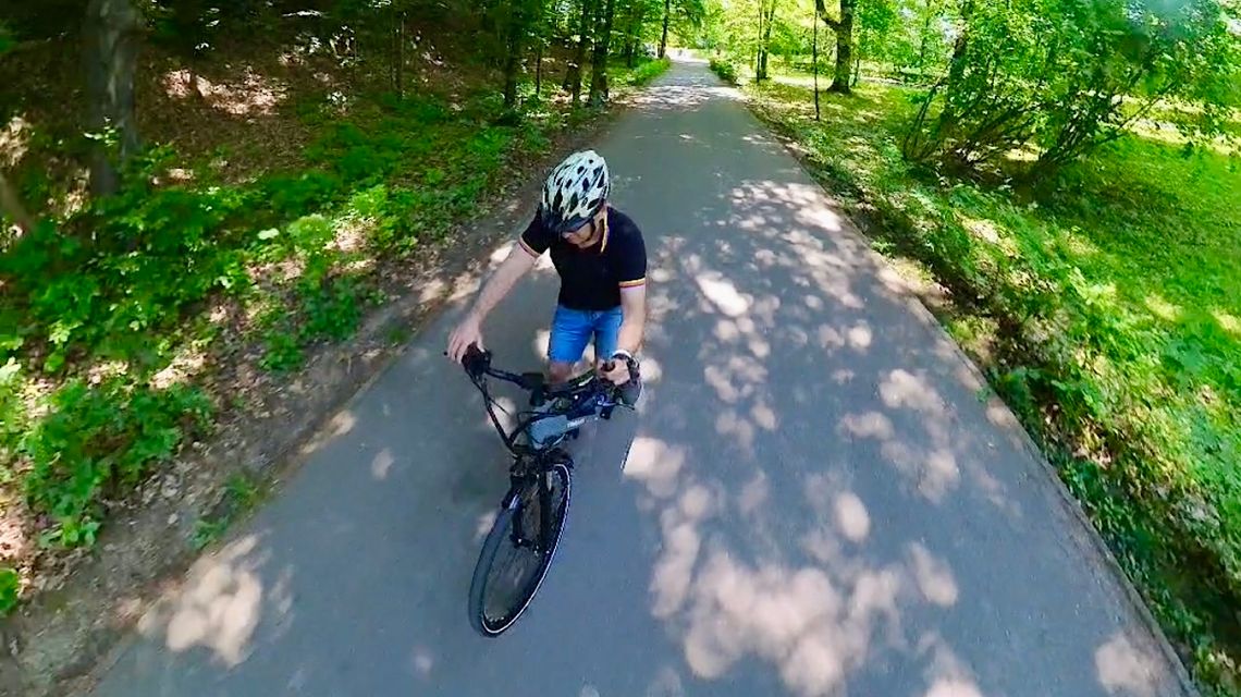 Mężczyzna jadący na rowerze w kasku. Jedzie przez park