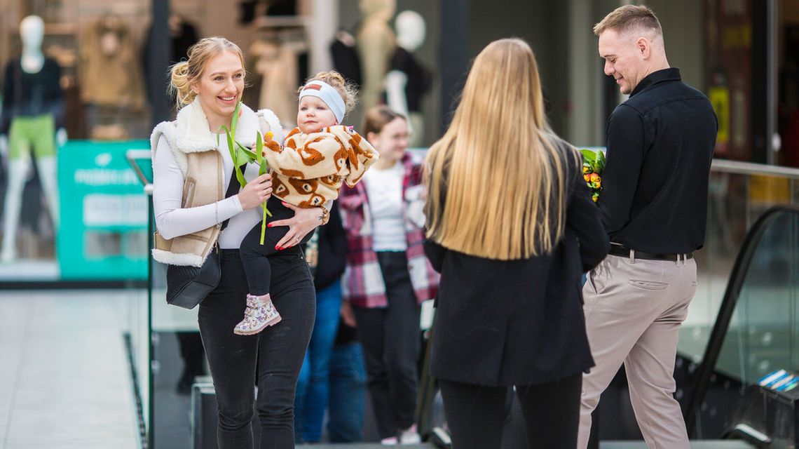 zdjęcie przedstawia kobietę z dzieckiem na ręku, w drugiej ręce trzyma tulipana