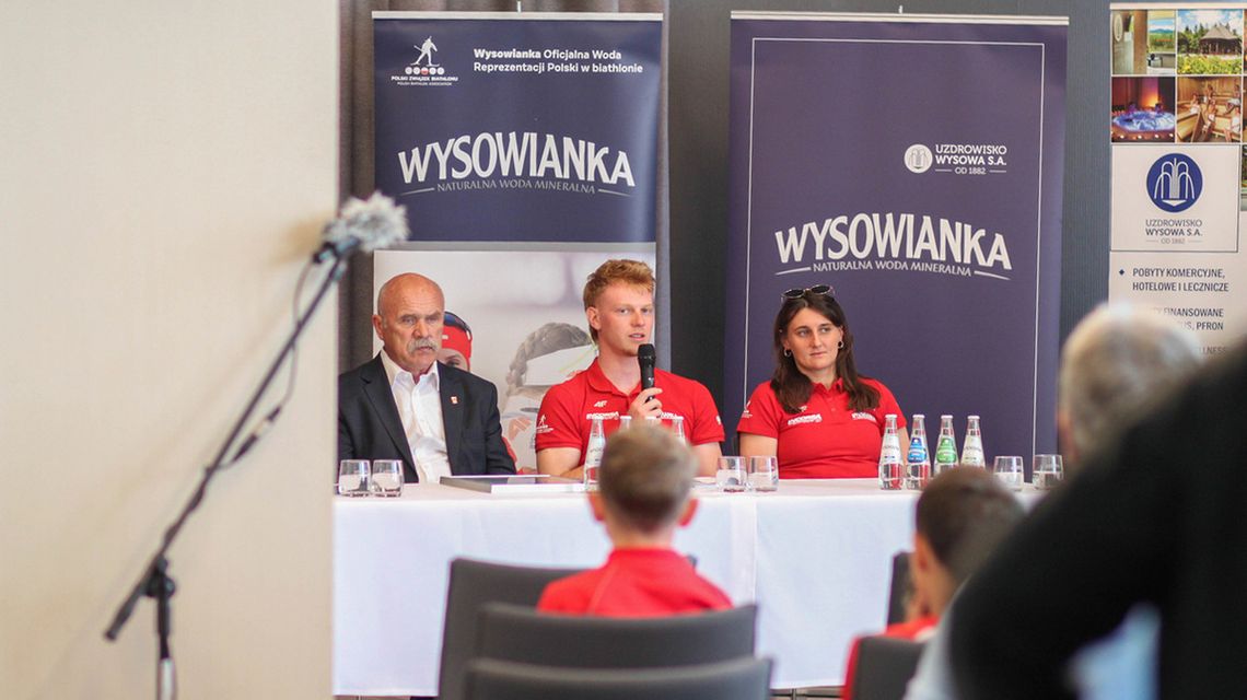 zdjęcie przedstawia osoby siedzące przy stole z mikrofonem