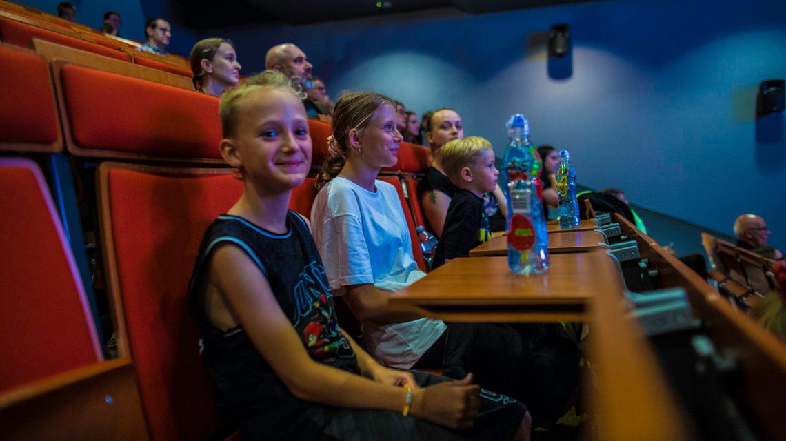 zdjęcie przedstawia dzieci siedzące w ławkach podczas prelekcji