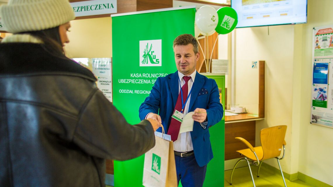 mężczyzna z w garniturze pod krawatem wręcza papierową torbę kobiecie