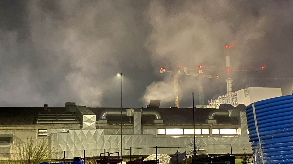 zdjęcie przedstawia dym wydobywający się z budynku, w tle komin i dźwig