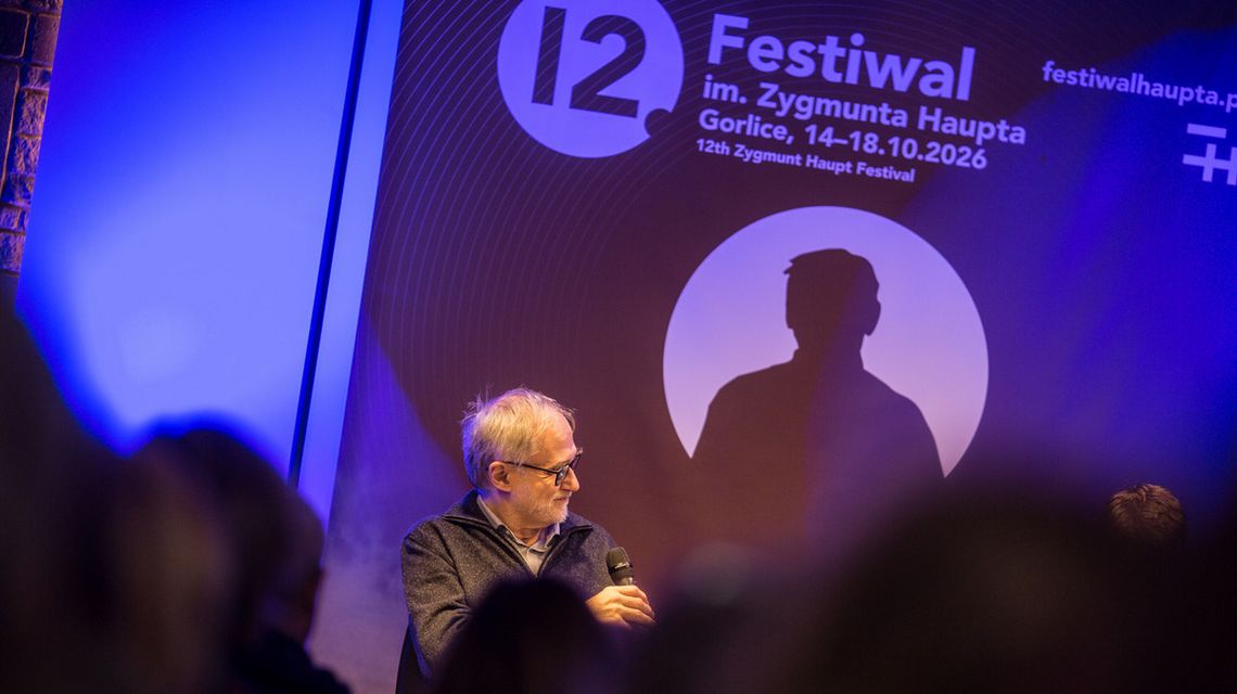 mężczyzna z mikrofonem na tle baneru 12. festiwal im. Z. Haupta w Gorlicach