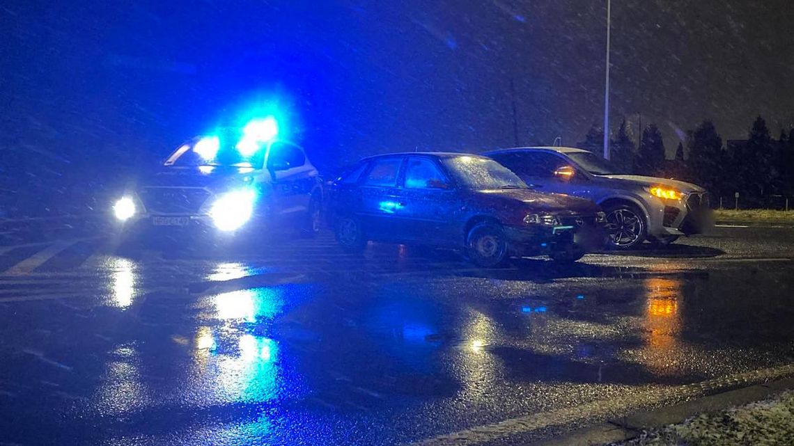 zdjęcie przedstawia uszkodzone pojazdy na jezdni, obok radiowóz policji z włączonymi sygnałami świetlnymi