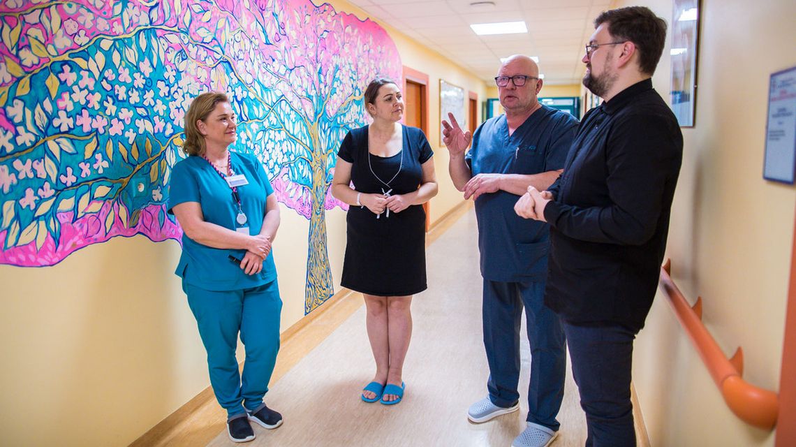 zdjęcie przedstawia cztery osoby stojące na korytarzu szpitala, na ścianie namalowane kolorowe drzewo