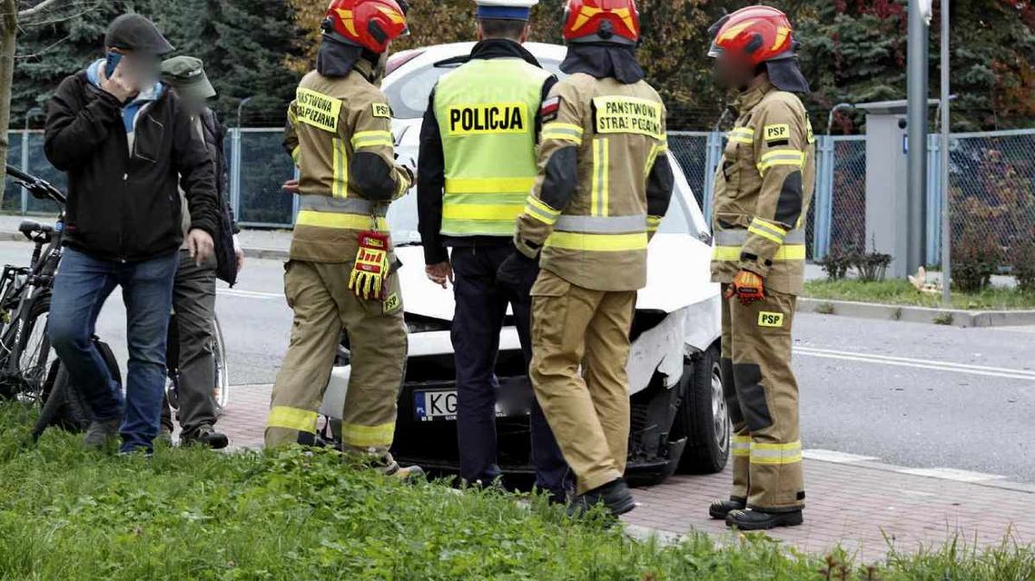 zdjęcie przedstawia uszkodzony pojazd a przed nim strażacy i policjanci