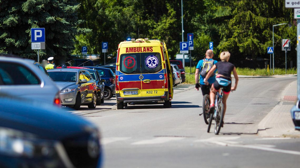 zdjęcie przedstawia karetkę pogotowia stojącą na jezdni obok policjant i rowerzyści