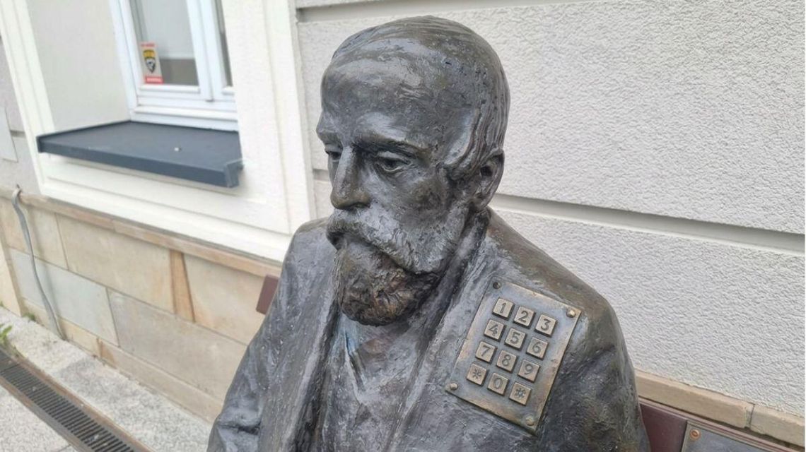 zdjęcie przedstawia posąg siedzący na ławce przed ratuszem w gorlicach