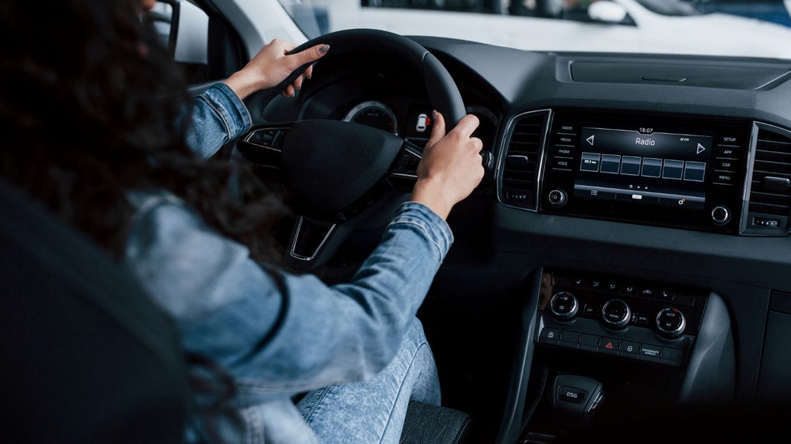 zdjęcie przedstawia kobietę siedzącą w samochodzie trzymającą ręce na kierownicy, widok z tylnego fotela