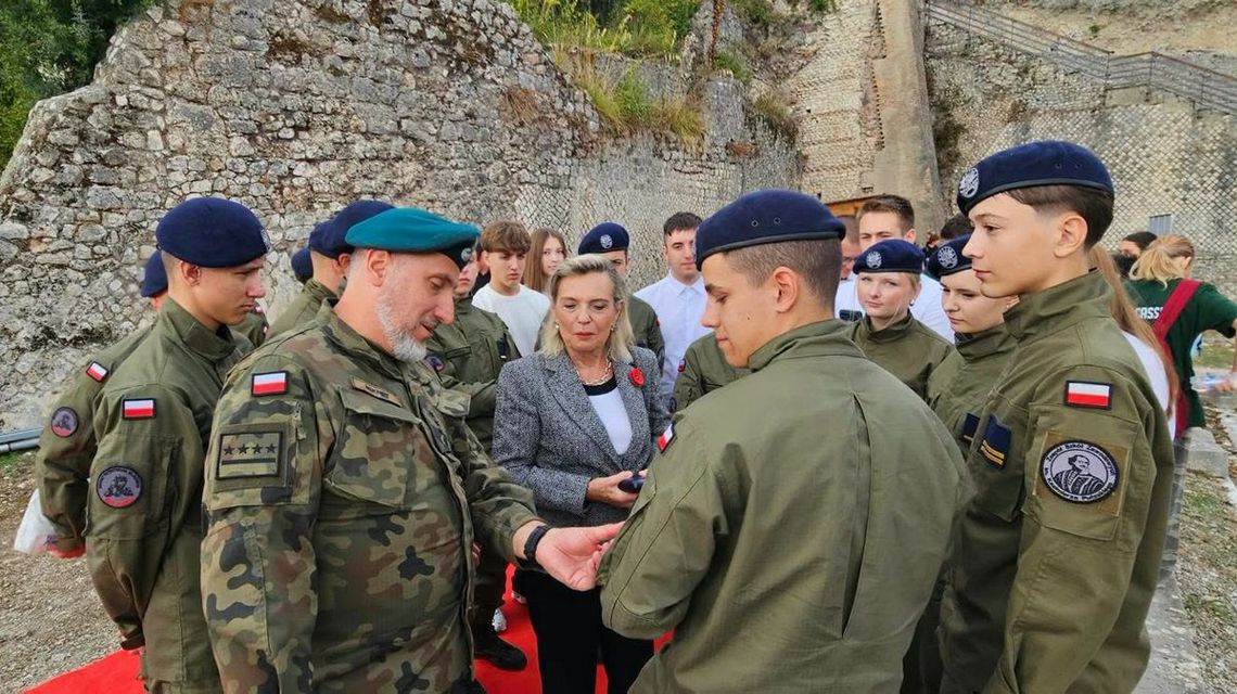 grupa osób w mundurach i z beretami wojskowymi, w tle mury i skały