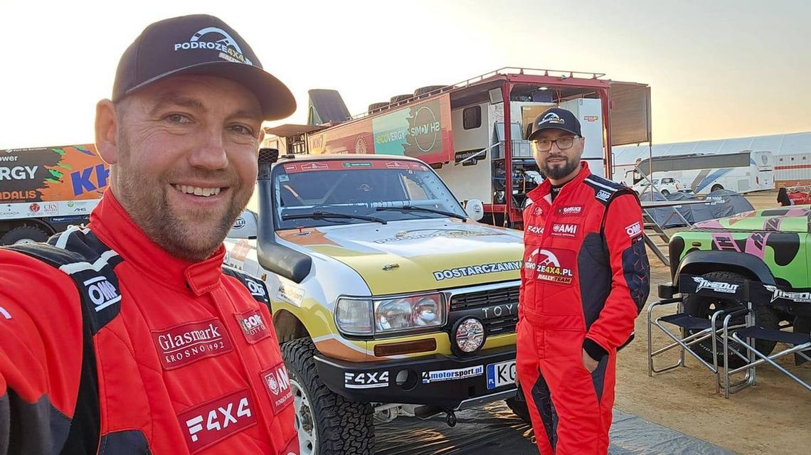 zdjęcie przedstawia dwóch mężczyzn w kombinezonach stojących przed autem rajdowym