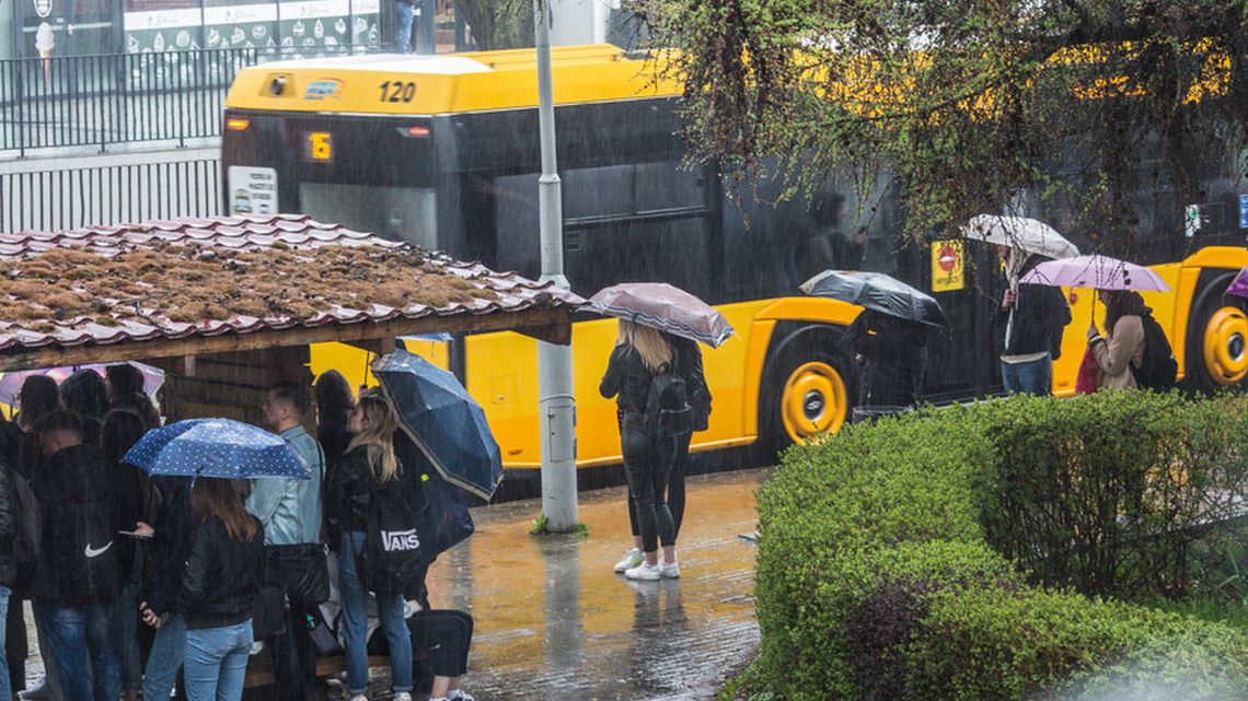 zdjęcie przedstawia przystanek autobusowy z czekającymi ludźmi pod parasolami