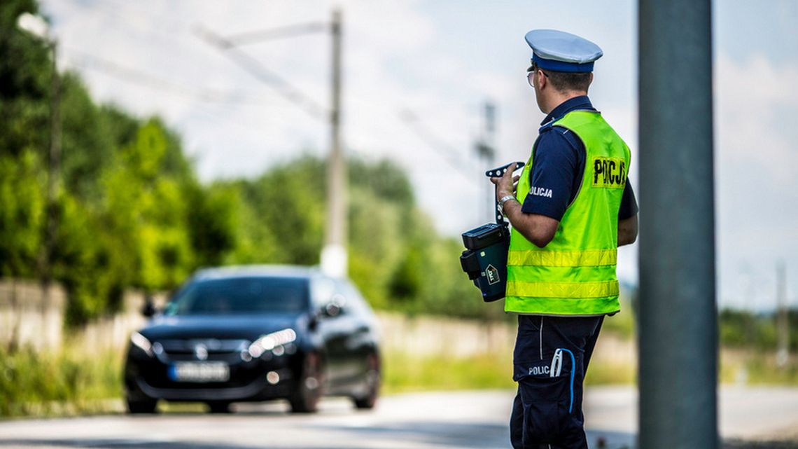 policjant z radarem stojący tyłem patrzący na jadący samochód