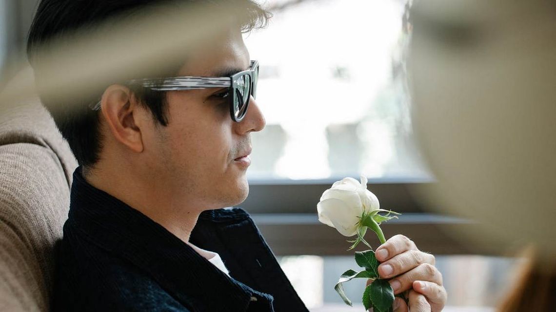 zdjęcie przedstawia mężczyznę w okularach z białym kwiatkiem w ręce