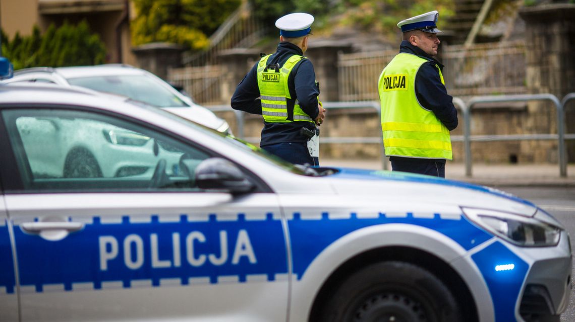 zdjęcie przedstawia policyjny radiowóz i dwóch policjantów stojących za nim
