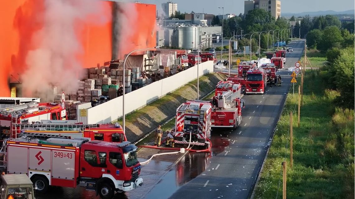 wozy strażackie stojące na ulicy przy hali z której wydobywa się dym