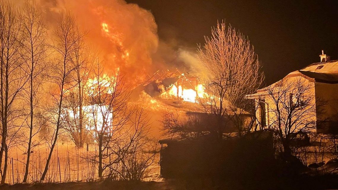 zdjęcie przedstawia płonący budynek za drzewami