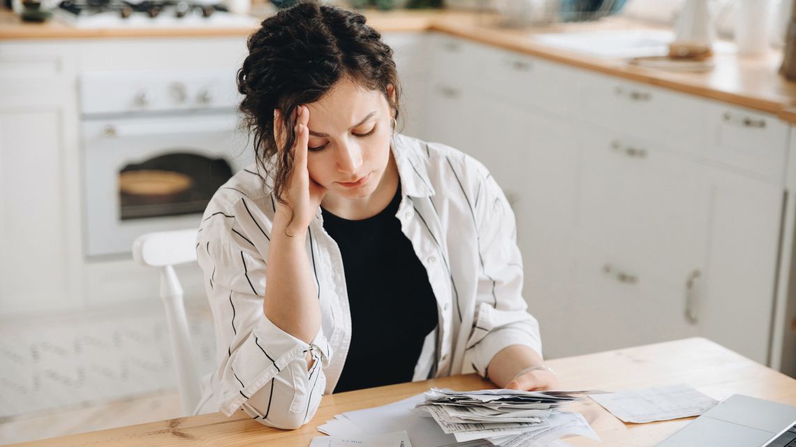 Mała pożyczka na remont mieszkania — ile i gdzie można pożyczyć? zdjęcie przedstawia kobietę siedzącą przy stole trzymającą w ręku rachunki