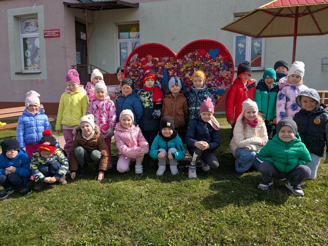 zdjęcie przedstawia grupę dzieci przed budynkiem szkolno przedszkolnym