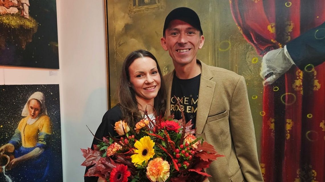 Karo i Mgr Mors z Nowego Sącza podczas otwarcia galerii sztuki, para stoi z kwiatami i uśmiecha się do obiektywu