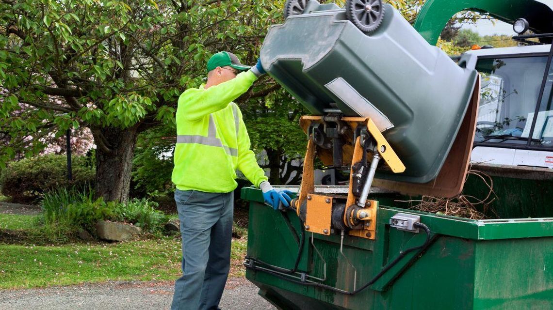 Mieszkańcy oczekują na informację, jak zmienią się opłaty za wywóz odpadów w gminie Gorlice? zdjęcie przedstawia mężczyznę, który wysypuje śmieci z kubła do śmieciarki