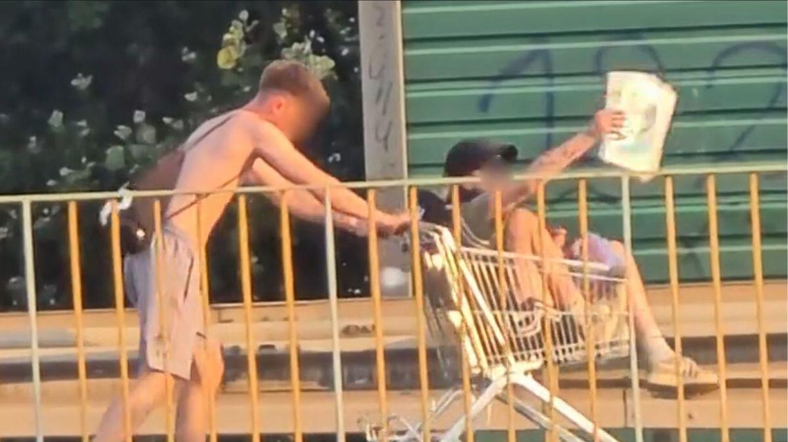 zdjęcie przedstawia chłopaka pchającego wózek sklepowy, w nim siedzi inna osoba