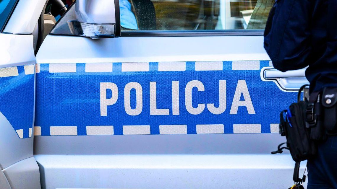 Drzwi policyjnego radiowozu z napisem policja, obok stoi policjant