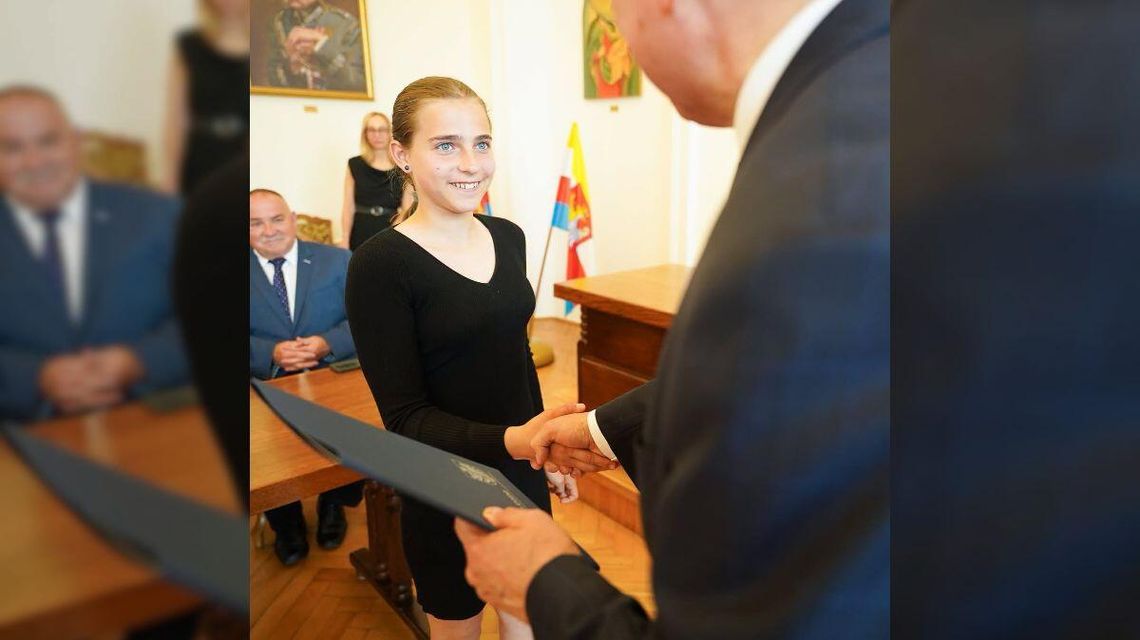 Nasza Zuzia z nagrodą Prezydenta Krosna zdjęcie przedstawia dziewczynę, której mężczyzna wręcza teczkę