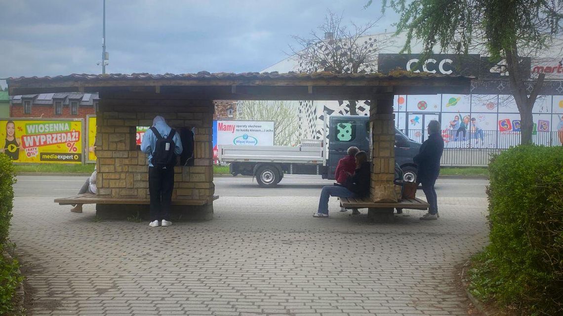 zdjęcie przedstawia przystanek autobusowy w gorlicach, na ławkach siedzi kilka osób
