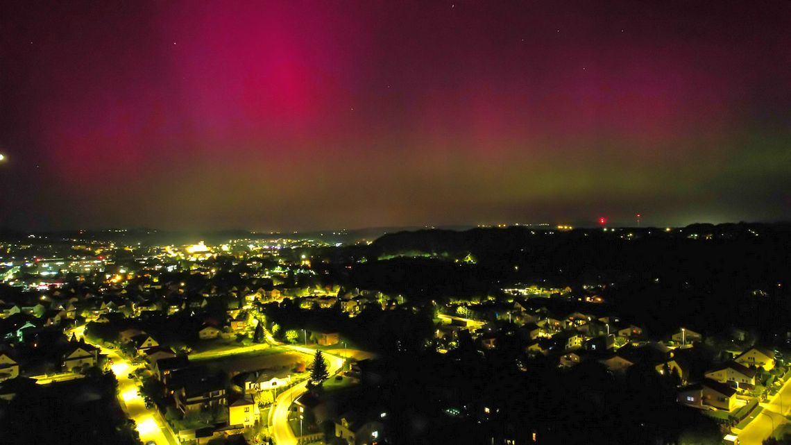 czerwone niebo od zorzy polarnej nad rozświetlonym od świateł ulicznych miastem w nocy