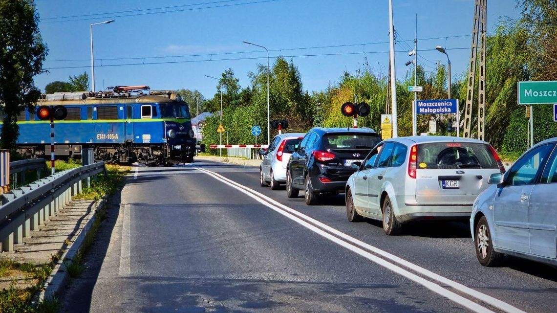 przejazd kolejowy w Moszczenicy przed którym stoją samochody i wjeżdża tam lokomotywa