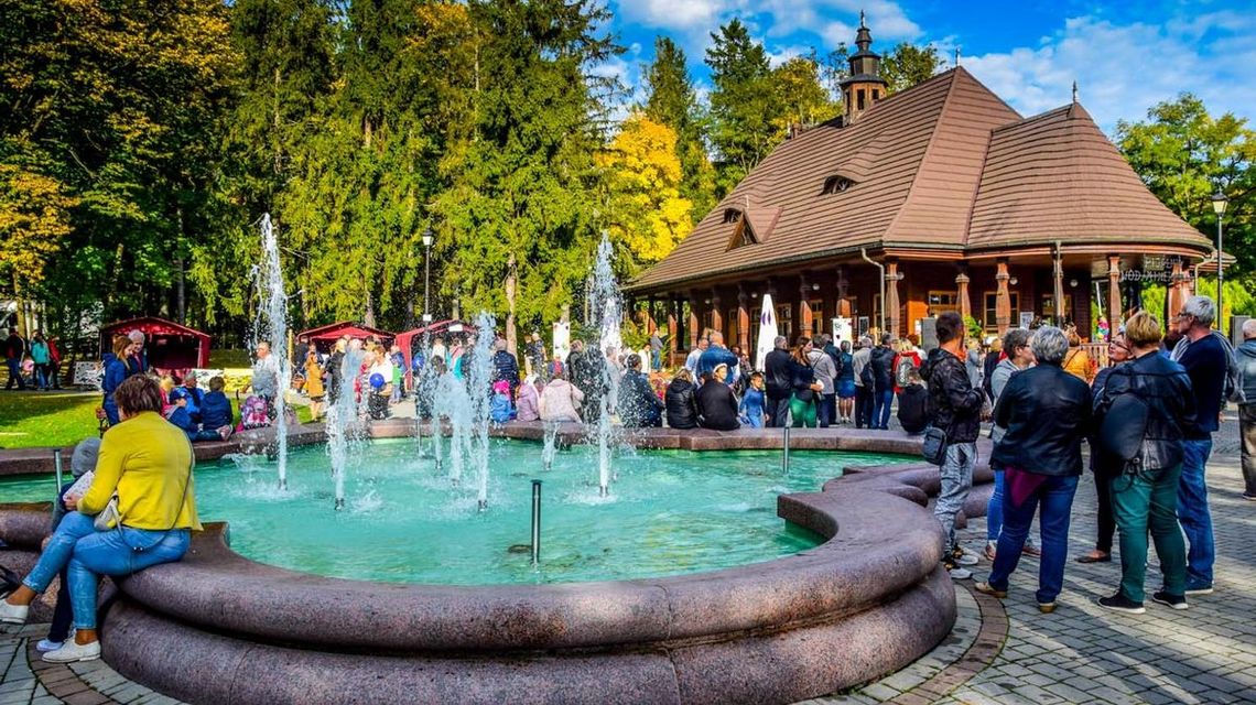 zdjęcie przedstawia fontannę i dom, obok stoją ludzie