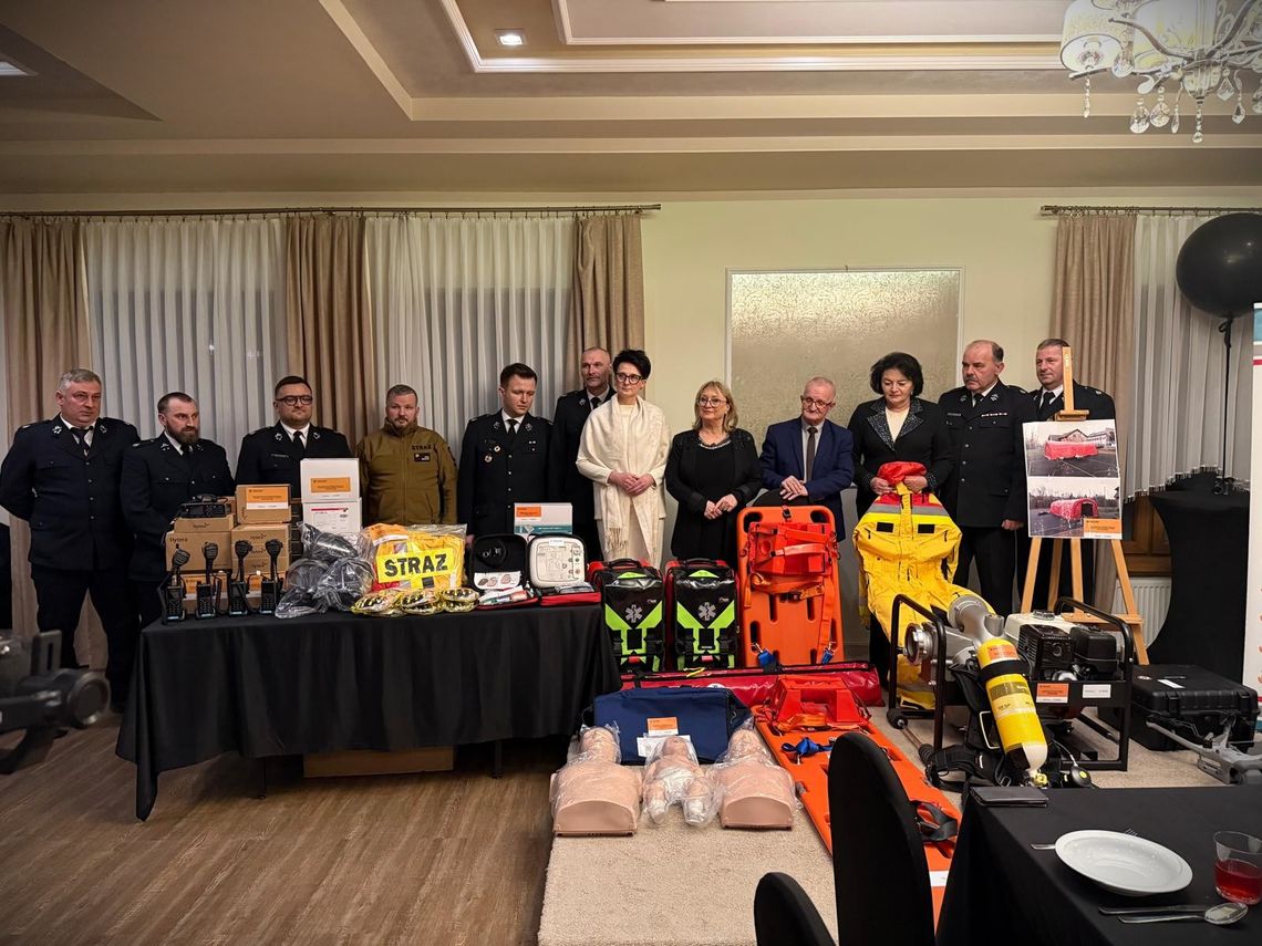 zdjęcie przedstawia grupę ludzi przy stole na którym leżą pakunki i urządzenia