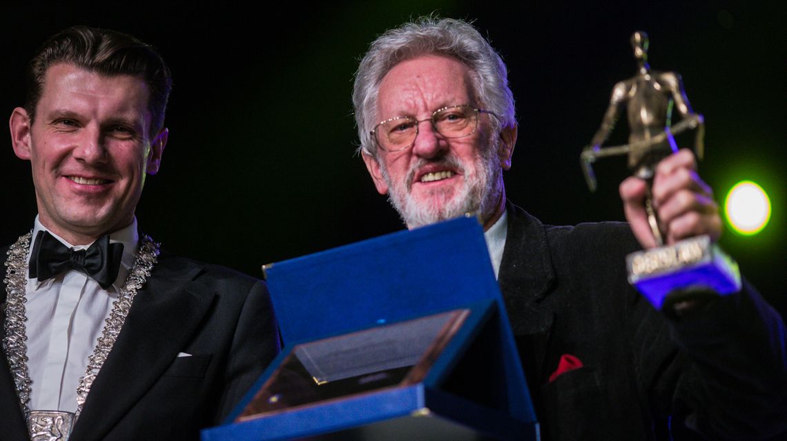 zdjęcie przedstawia dwóch mężczyzn, jeden trzyma statuetkę