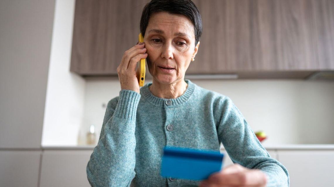 zdjęcie przedstawia kobietę, która trzyma w ręce kartę płatniczą, w drugiej ręce ma telefon przy uchu