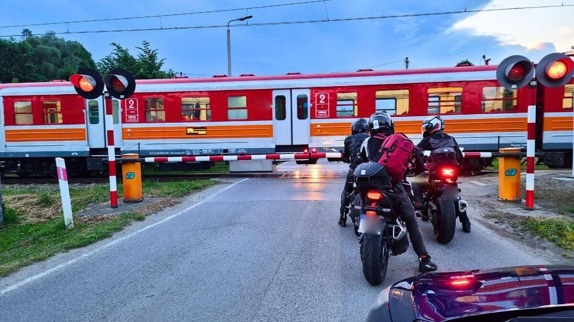 przejeżdżający pociąg przez przejazd kolejowy, samochody i motocykliści czekają przed szlabanem