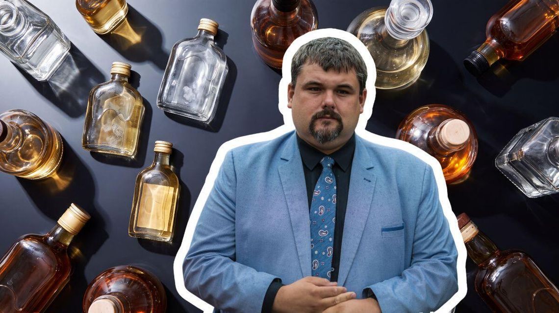 mężczyzna w garniturze na tle małych butelek z alkoholem