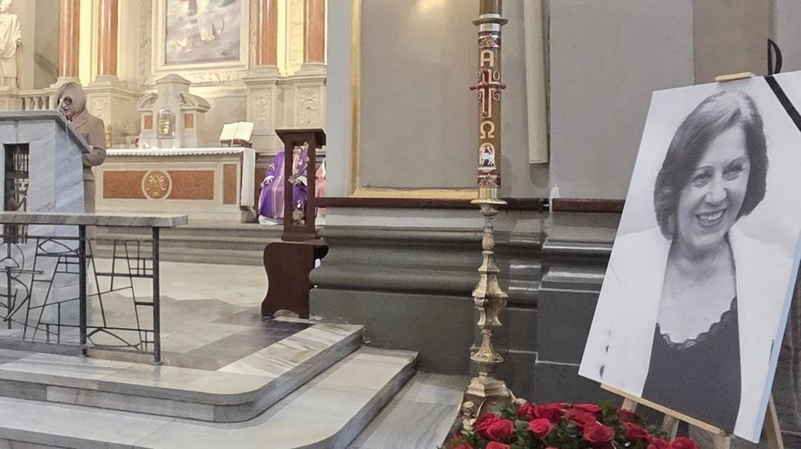 zdjęcie przedstawia wnętrze kościoła, na posadce stoi portret kobiety, w głębi ołtarz i stojąca kobieta przy pulpicie