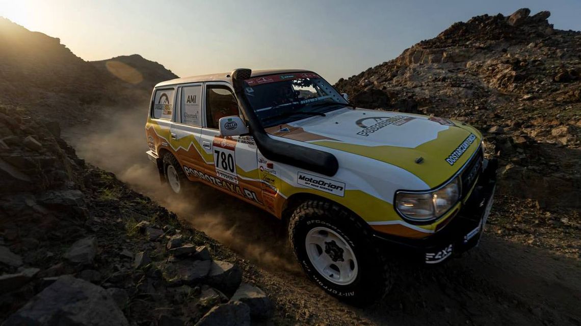 zdjęcie przedstawia samochód rajdowy jadący po pustyni między głazami