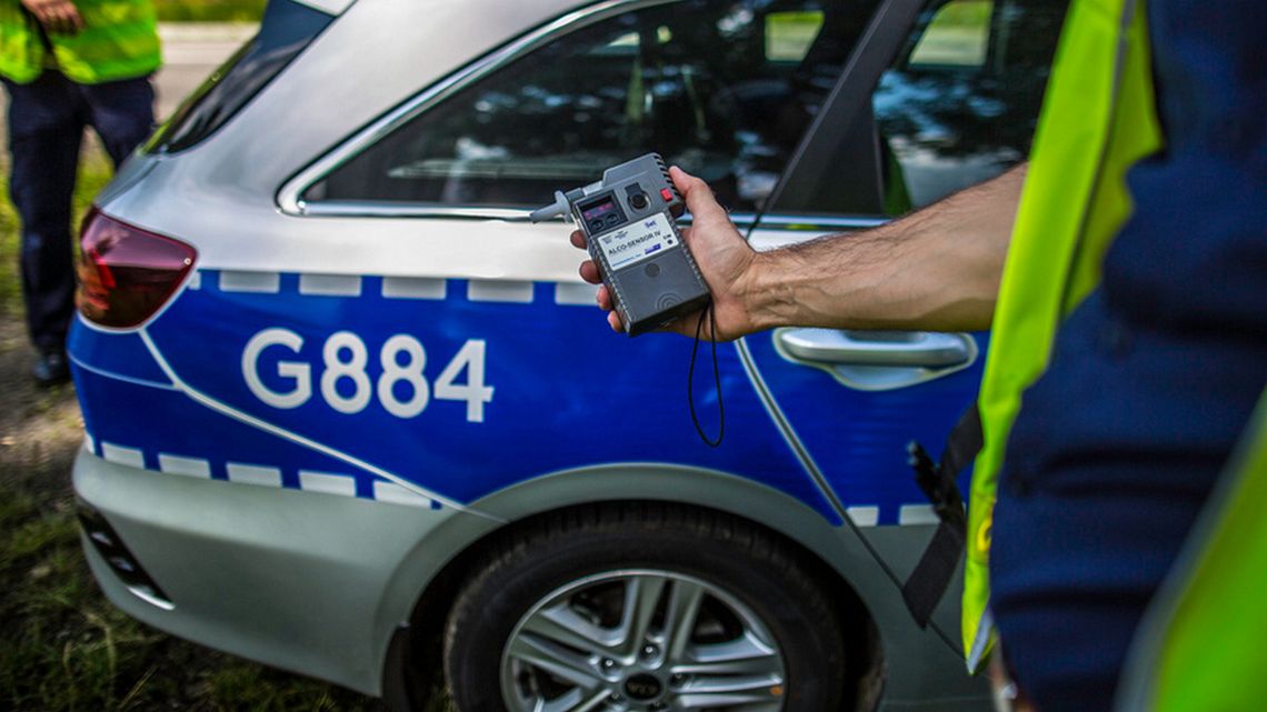 alkomat trzymany w ręce przez policjanta, w tle radiowóz