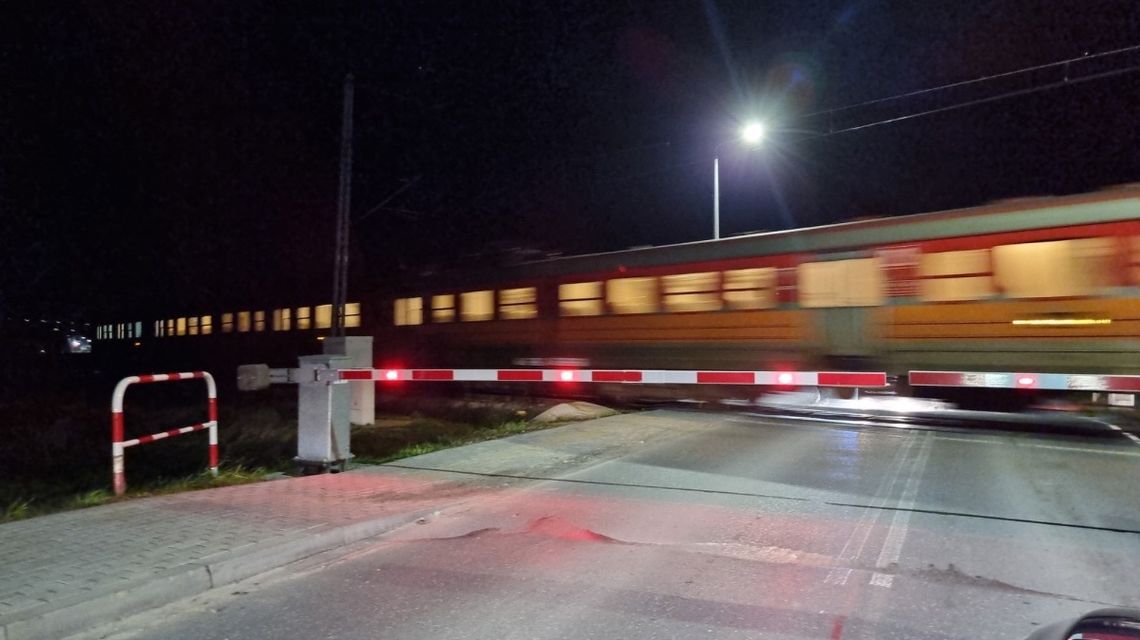 Pociąg jadący po torach nocą szlabany opuszczone