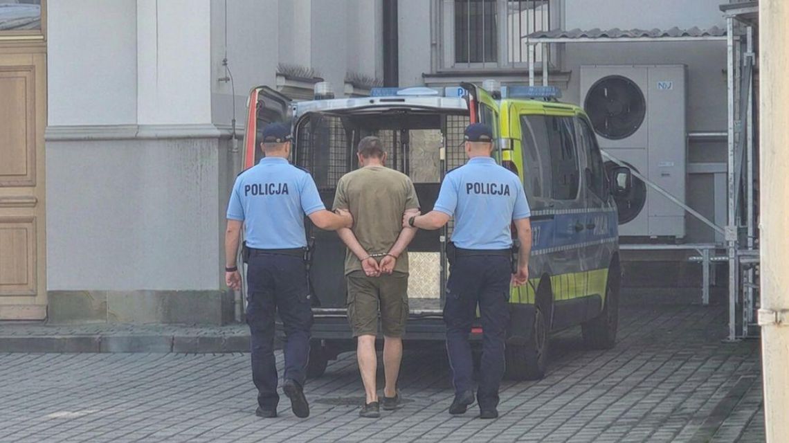 Podejrzany o atak w Zdyni Ukrainiec był przesłuchany w gorlickiej prokuraturze zdjęcie przedstawia policjantów prowadzących zatrzymanego, w kajdankach, przed radiowozem