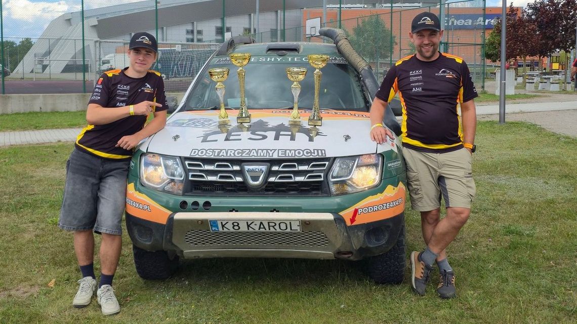 Podwójny triumf gorliczanina w Baja Poland. Mariusz Pietrzycki zwyciężył razem z synem dwóch mężczyzn przy samochodzie, na jego masce stoją puchary