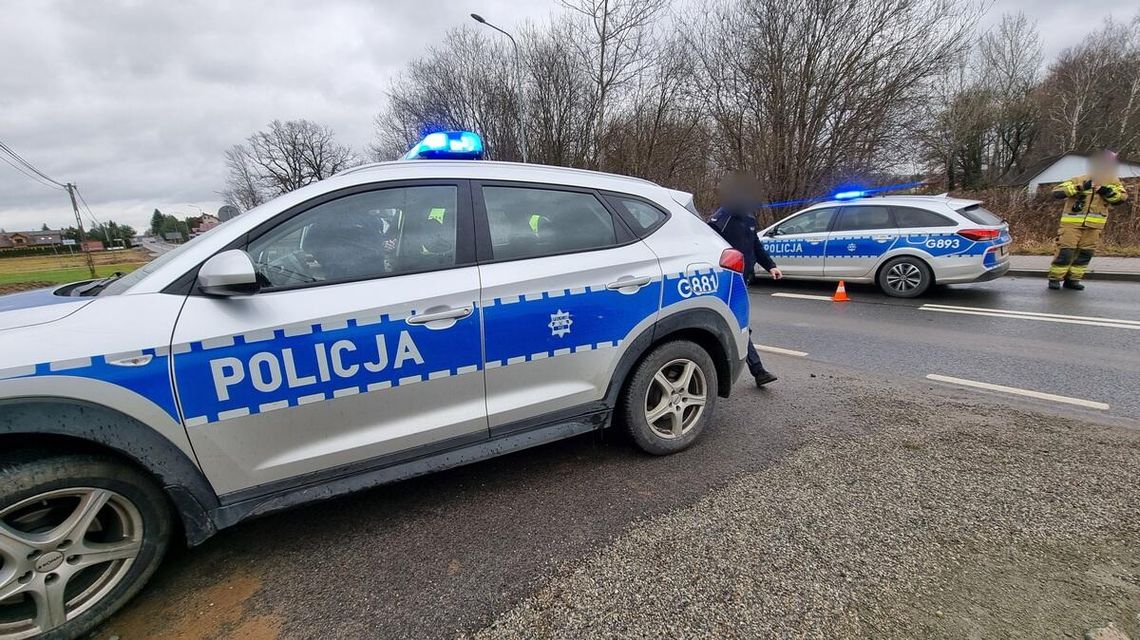 zdjęcie przedstawia dwa radiowozy policji, obok policjant i strażak