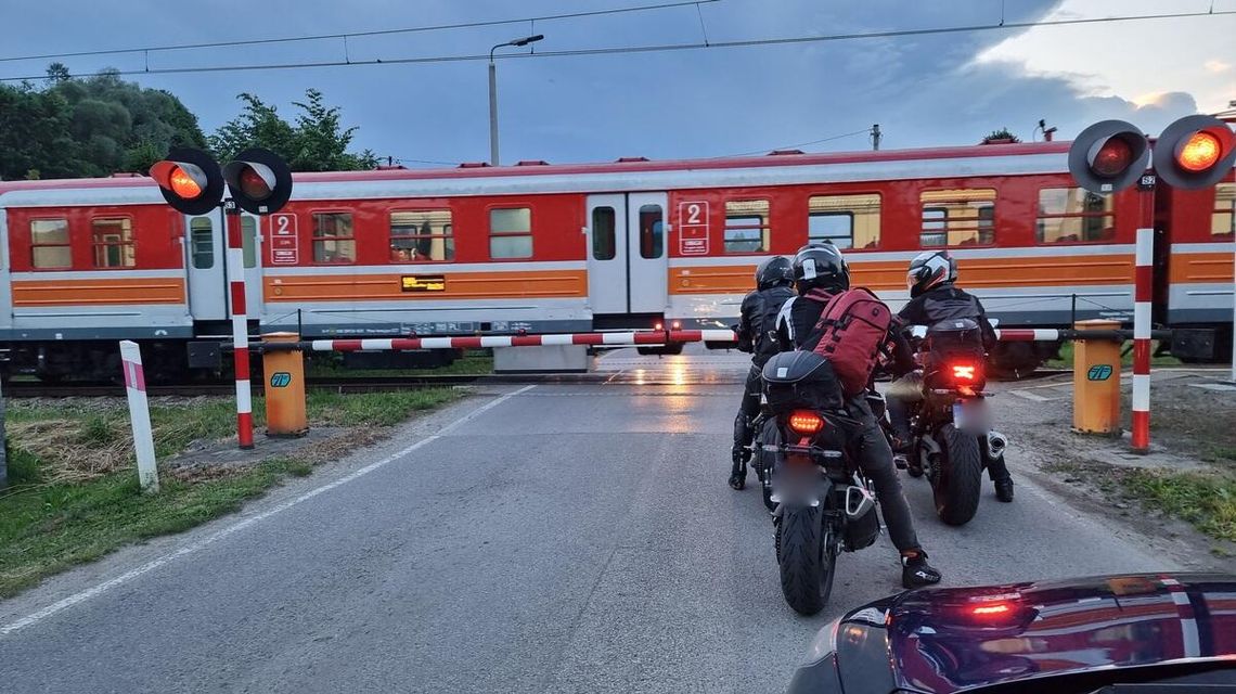 zdjęcie przedstawia pociąg przejeżdżający przez przejazd kolejowy, przed którym stoją motocykle