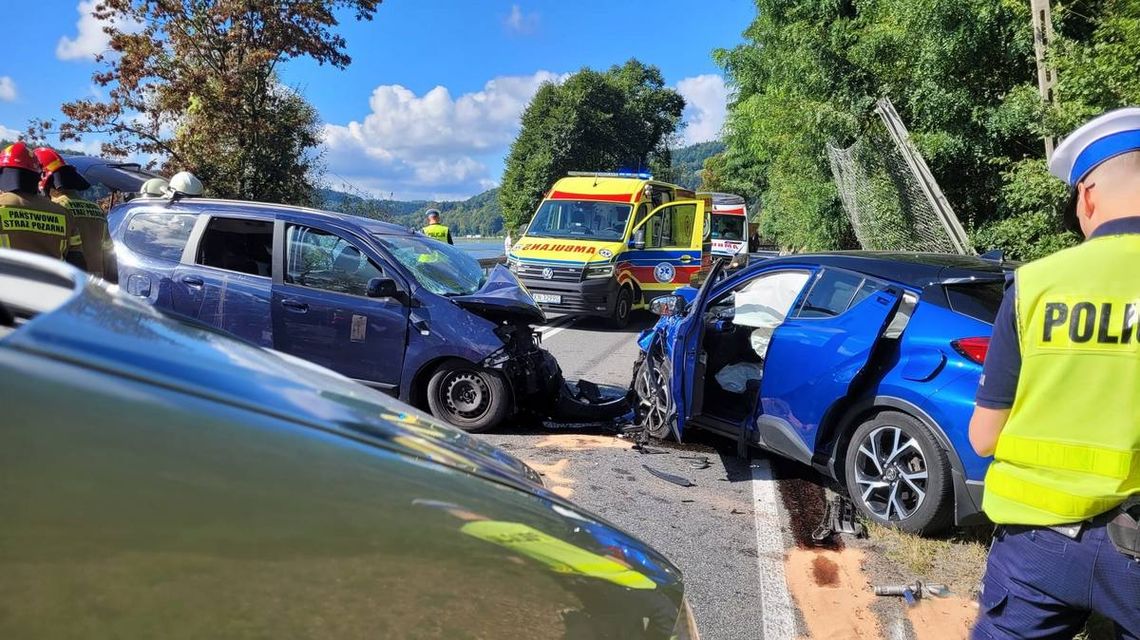 scena z wypadku drogowego, w centralnym punkcie zdjecia dwa pojazdy w kolorze granatowym, w tle widoczny żółty ambulans