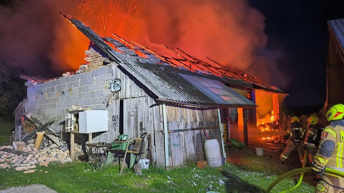zdjęcie przedstawia spalony budynek gospodarczy, obok strażacy, zdjęcie w nocy